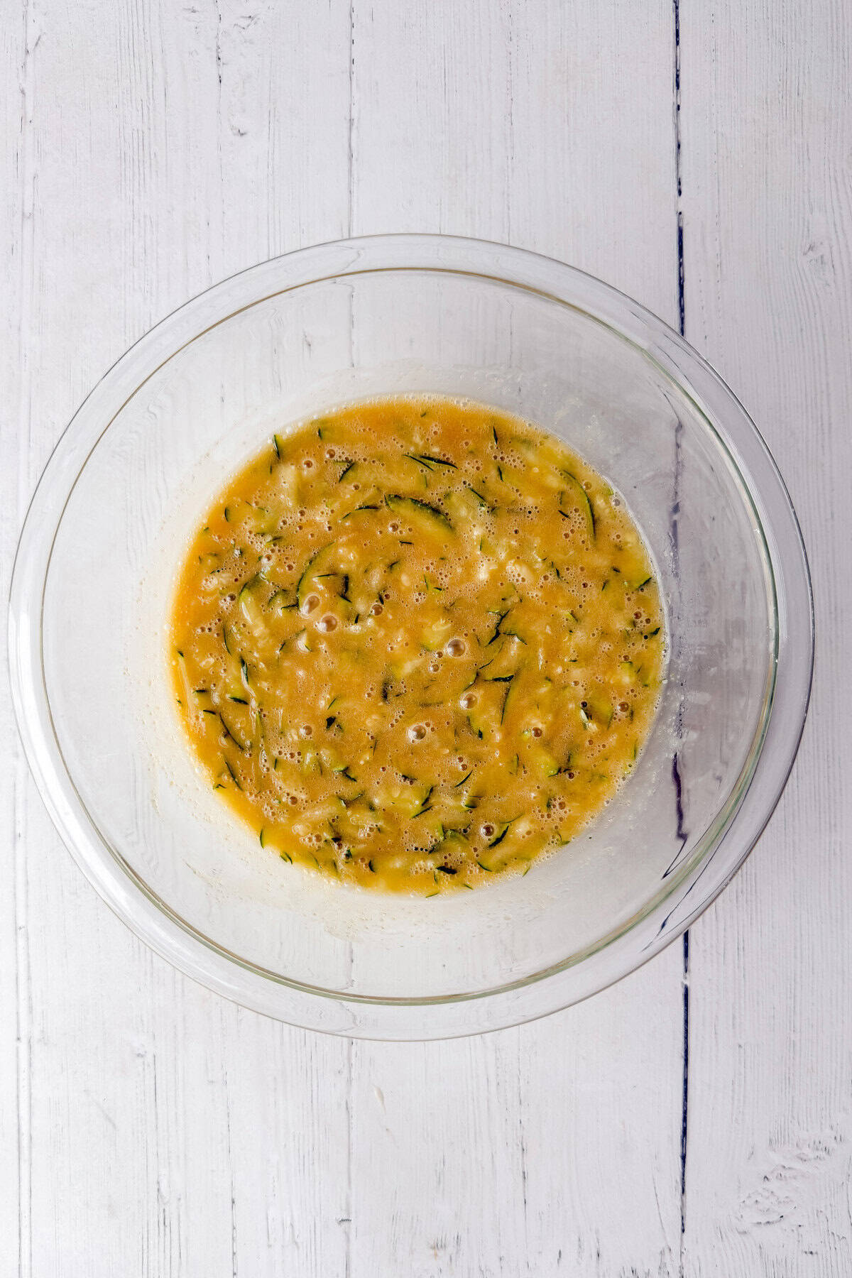 Eggs, sugar, oil, sour cream, and grated zucchini whisked together in a glass bowl for easy zucchini bread, no mixer required.