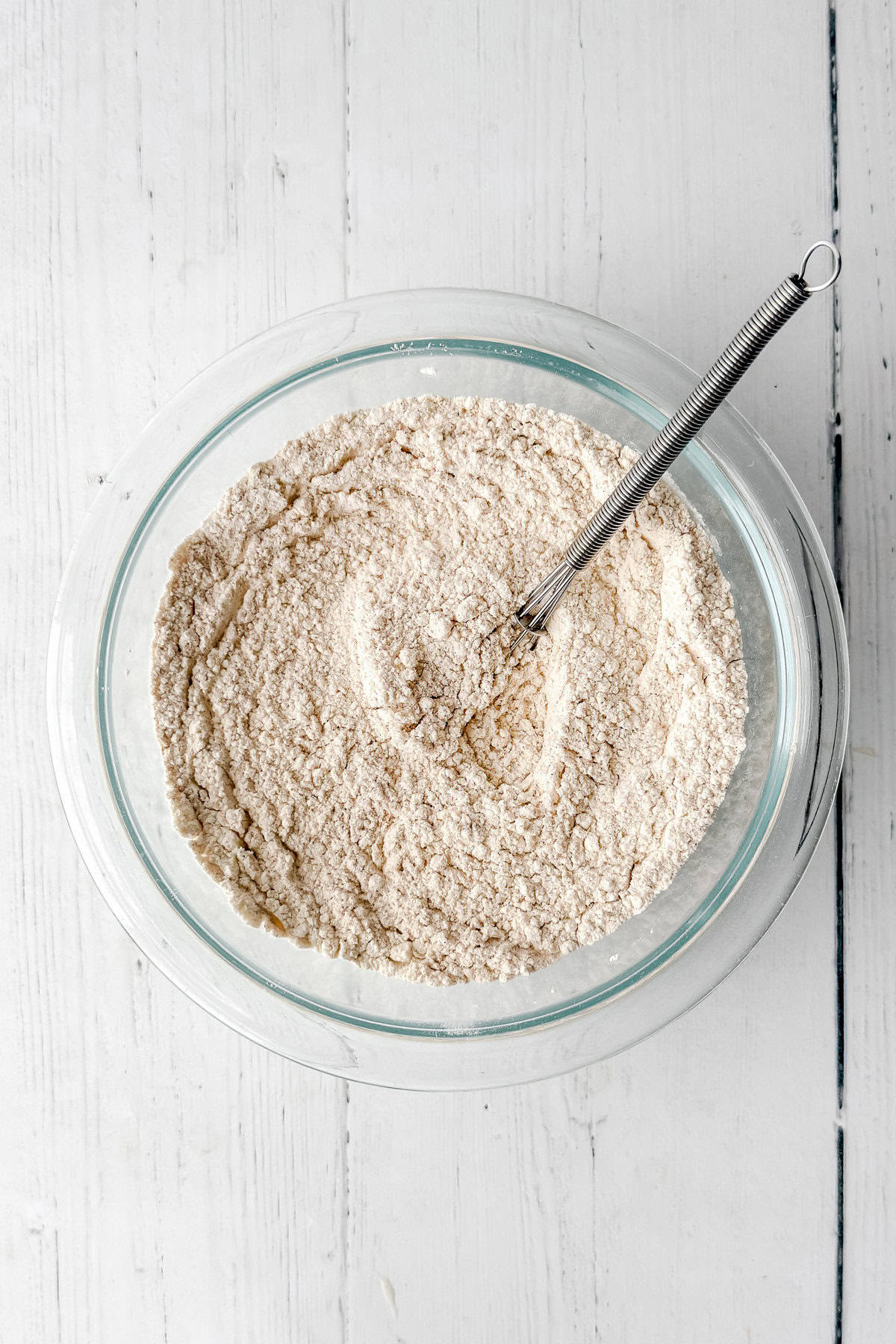 Glass bowl with flour, baking soda, baking powder, salt, and spices being whisked for single loaf zucchini bread recipe.