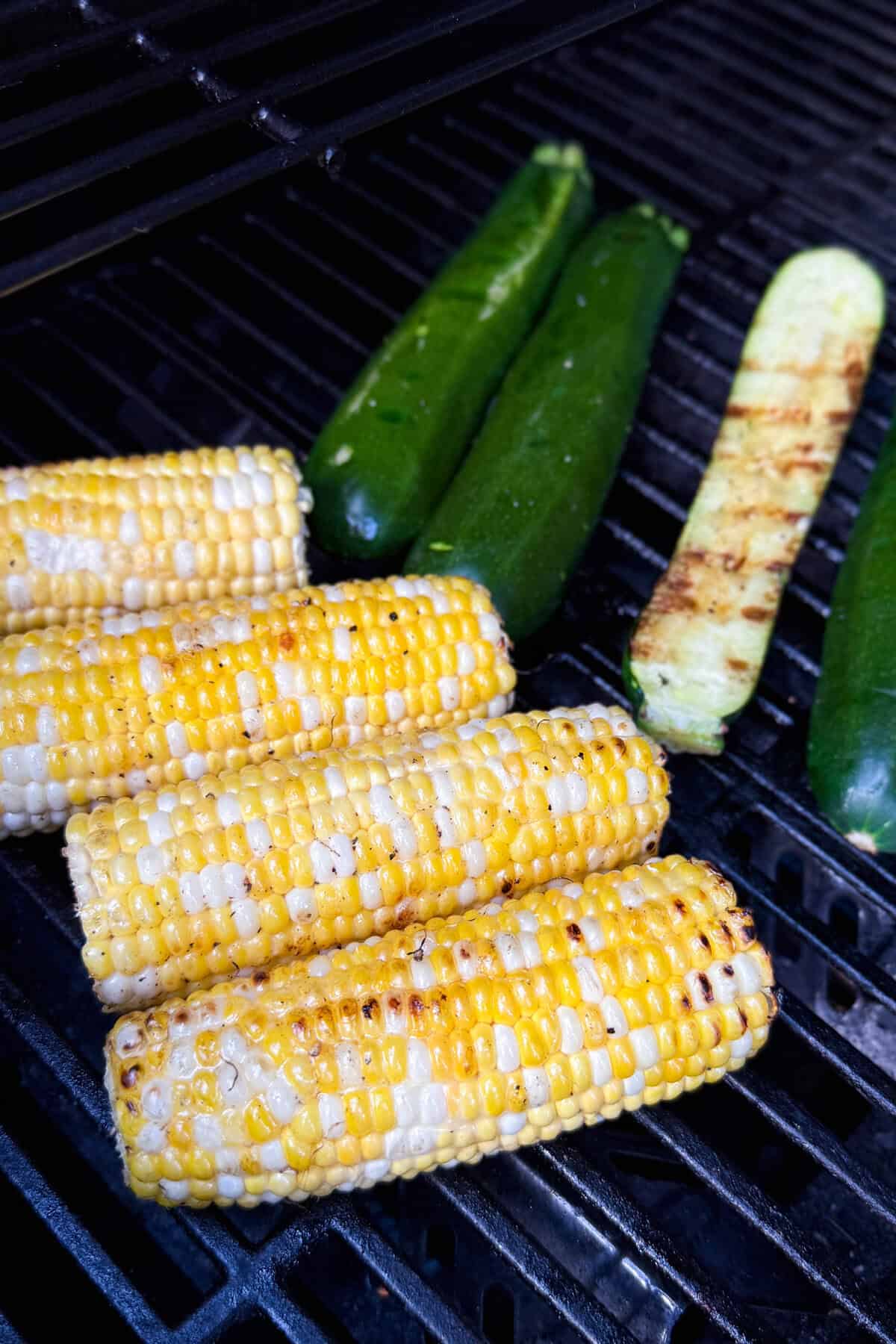 Corn on the cob and grilled zucchini are sizzling on a barbecue, with beautiful grill marks-perfect for a fresh Grilled Zucchini Salad or a vibrant Corn Salad.