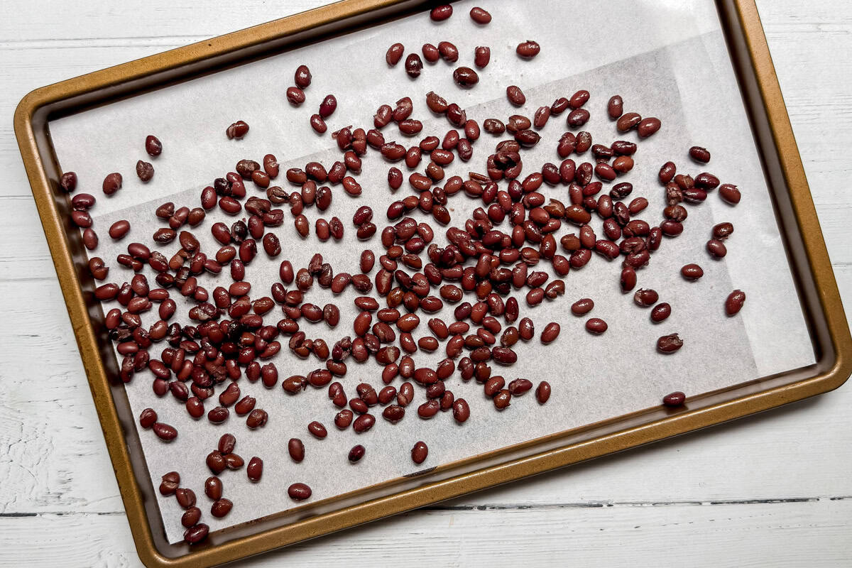 Black beans scattered on a parchment-lined baking sheet, placed on a white wooden surface.