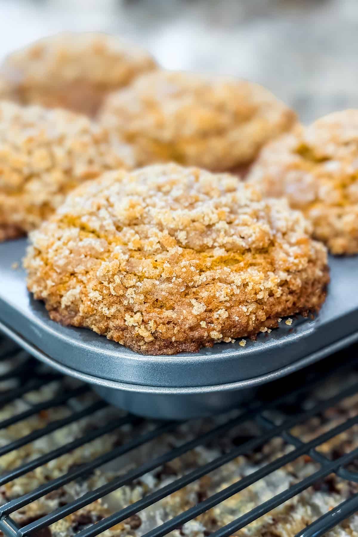 Close-up of crumb-topped Panera Pumpkin Muffins in a baking tray, cooling on a wire rack.