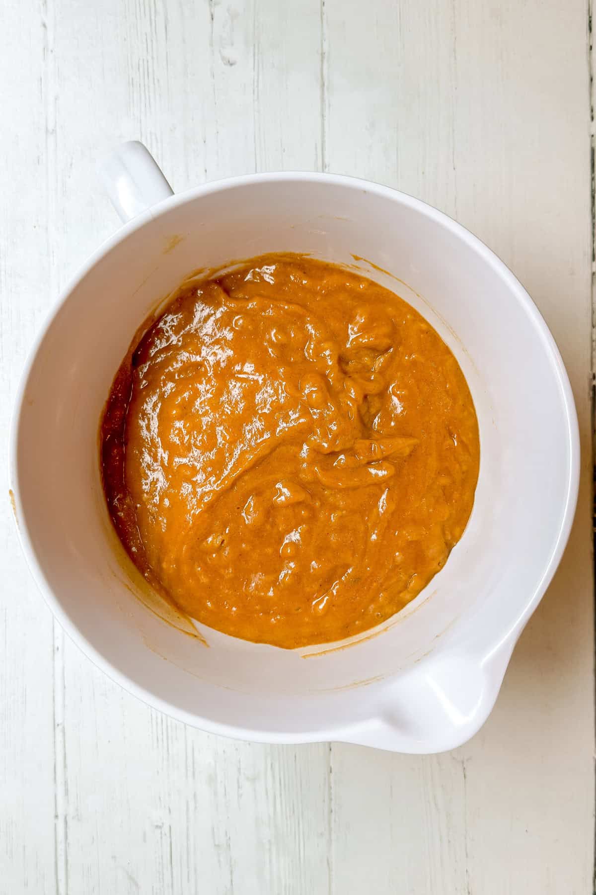 A white mixing bowl filled with thick, orange pumpkin muffin batter sits on a white wooden surface, reminiscent of Panera's seasonal treats.