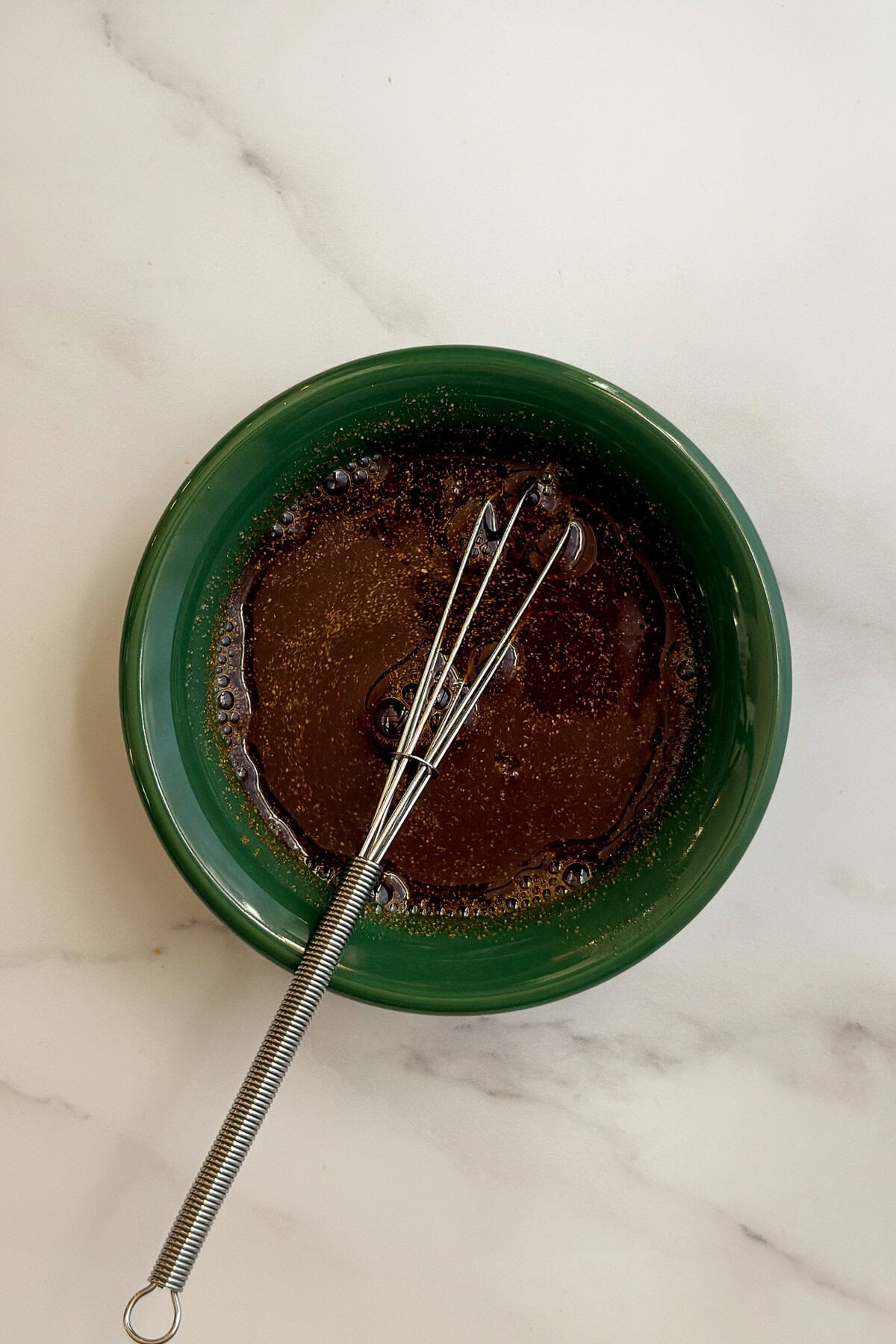 Green bowl with whisk and a dark teriyaki-style marinade of soy sauce, lemon, honey, ginger, and garlic.