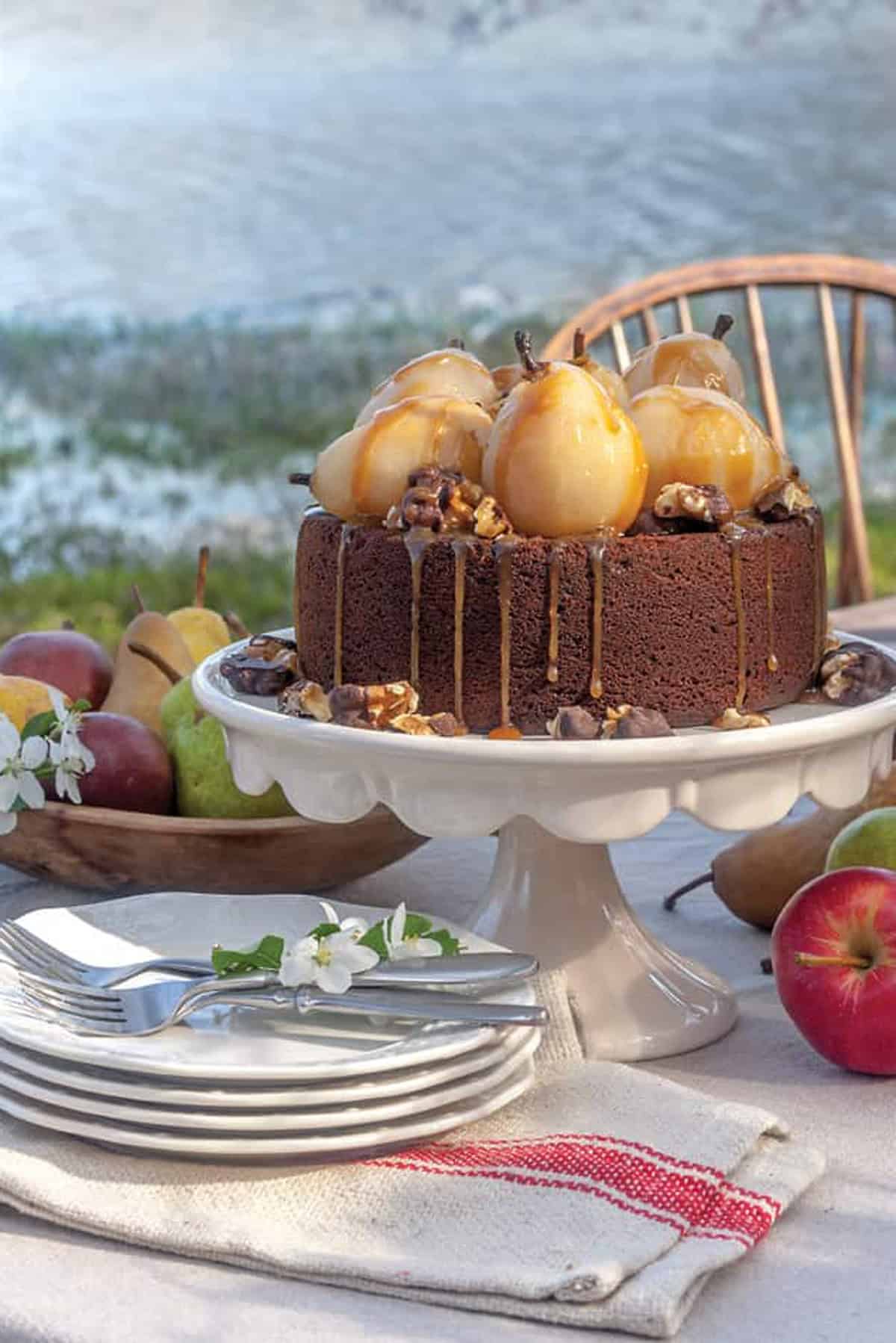 Cake topped with poached pears, caramel sauce, and nuts on a white cake stand.