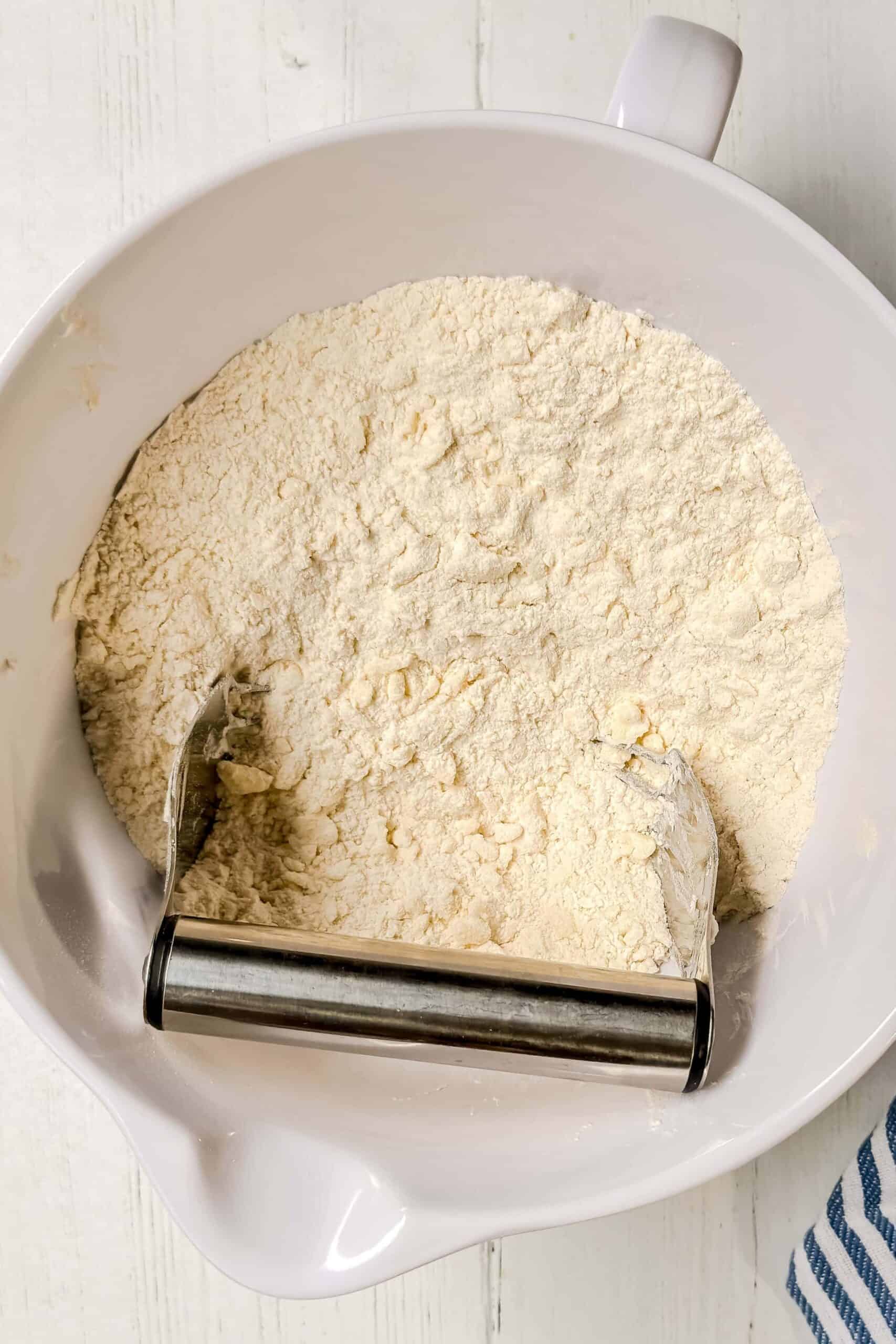 Top view of butter cut into flour with a pastry cutter in a white mixing bowl.