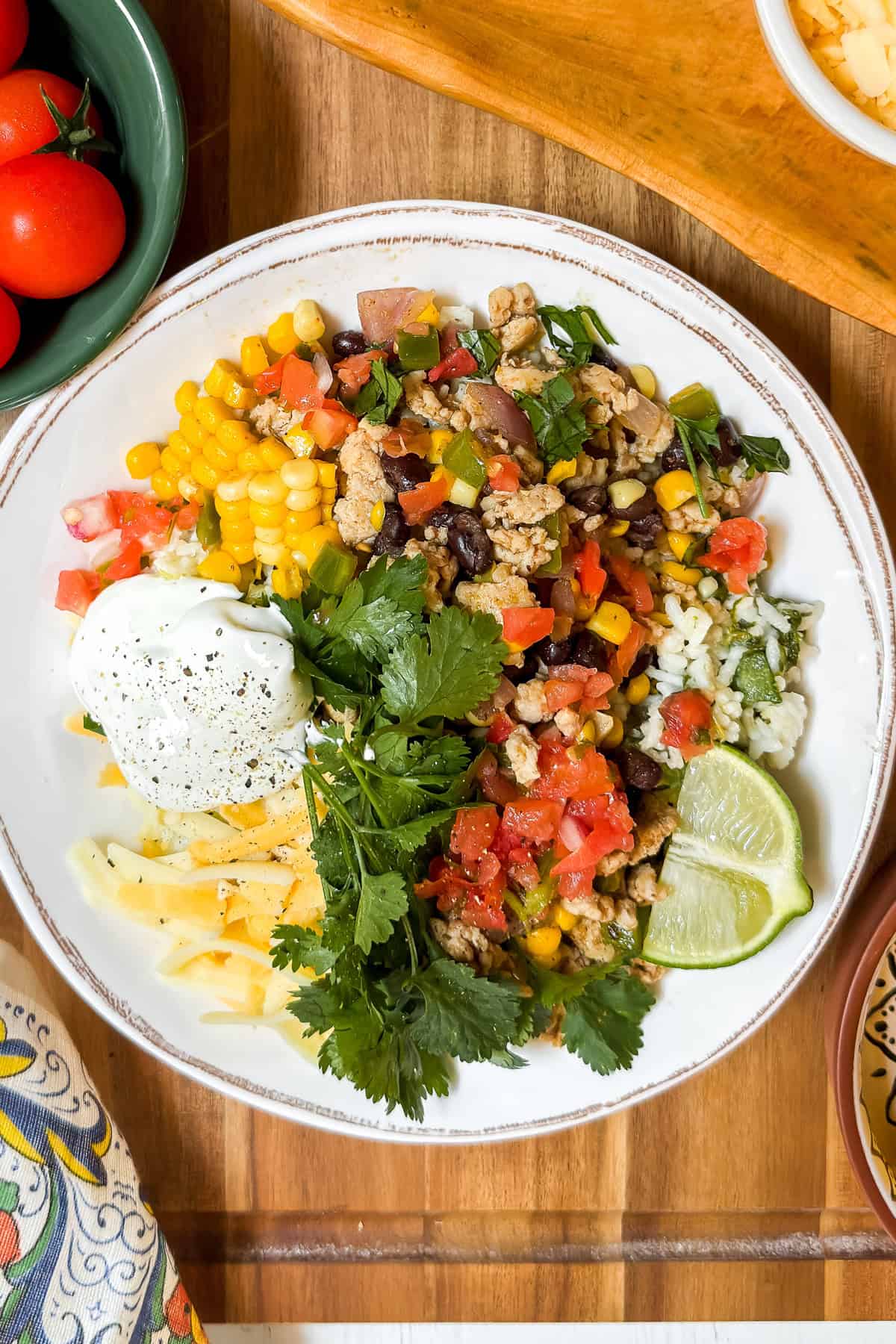 A white plate with ground meat, corn, black beans, rice, shredded cheese, salsa, sour cream, cilantro, and lime wedges arranged in sections—perfect for easy Chicken Taco Bowls.
