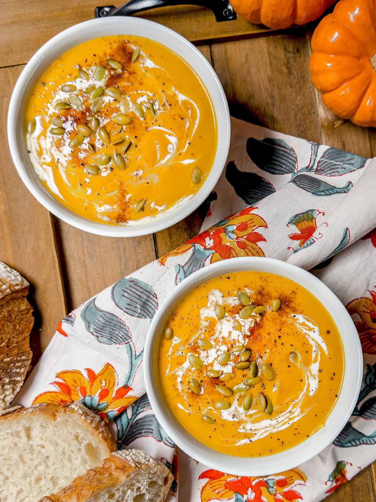 Two bowls of autumn squash pumpkin soup, topped with cream, pumpkin seeds, and seasoning.