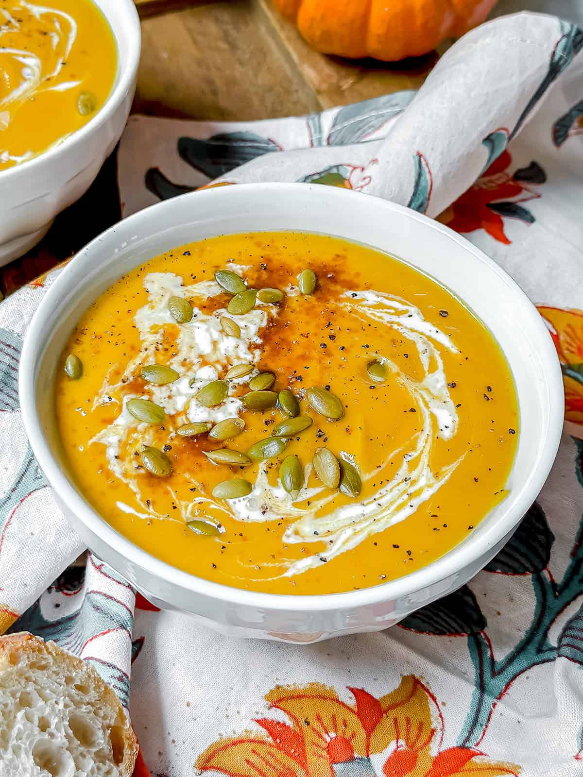 A bowl of creamy Panera Autumn Squash Soup, topped with pepitas, black pepper, and a swirl of cream.