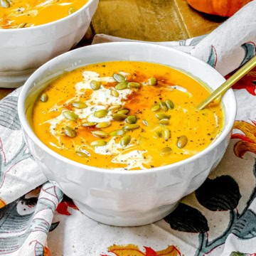 Bowl of Panera-inspired autumn squash soup topped with pepitas, cream, and black pepper.