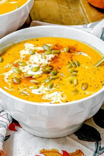 Bowl of Panera-inspired autumn squash soup topped with pepitas, cream, and black pepper.