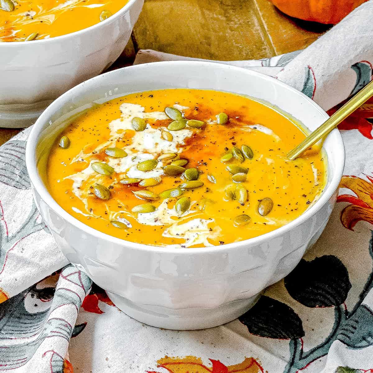 Bowl of Panera-inspired autumn squash soup topped with pepitas, cream, and black pepper.