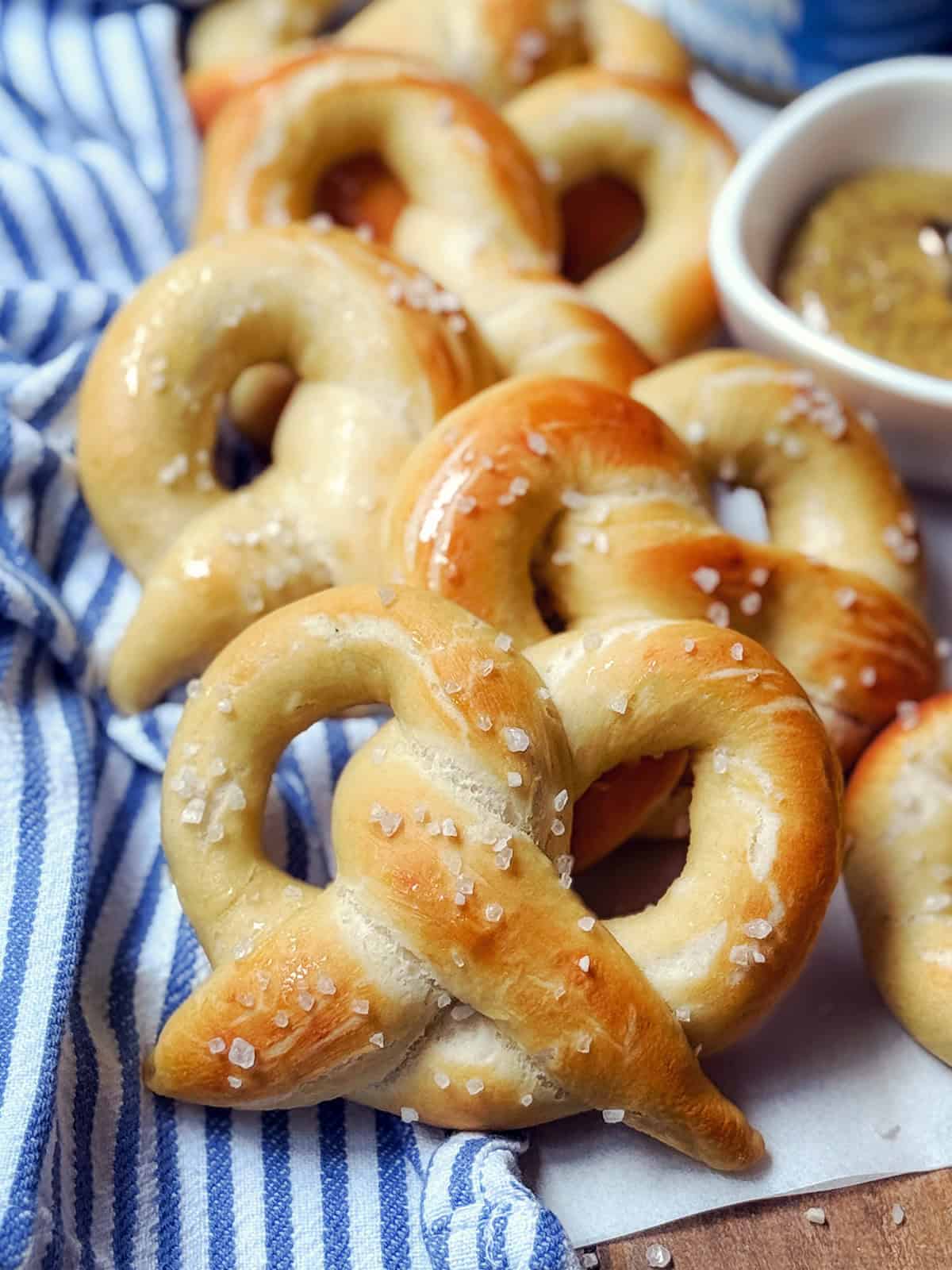 Stack of homemade soft pretzels with grainy mustard in the background.