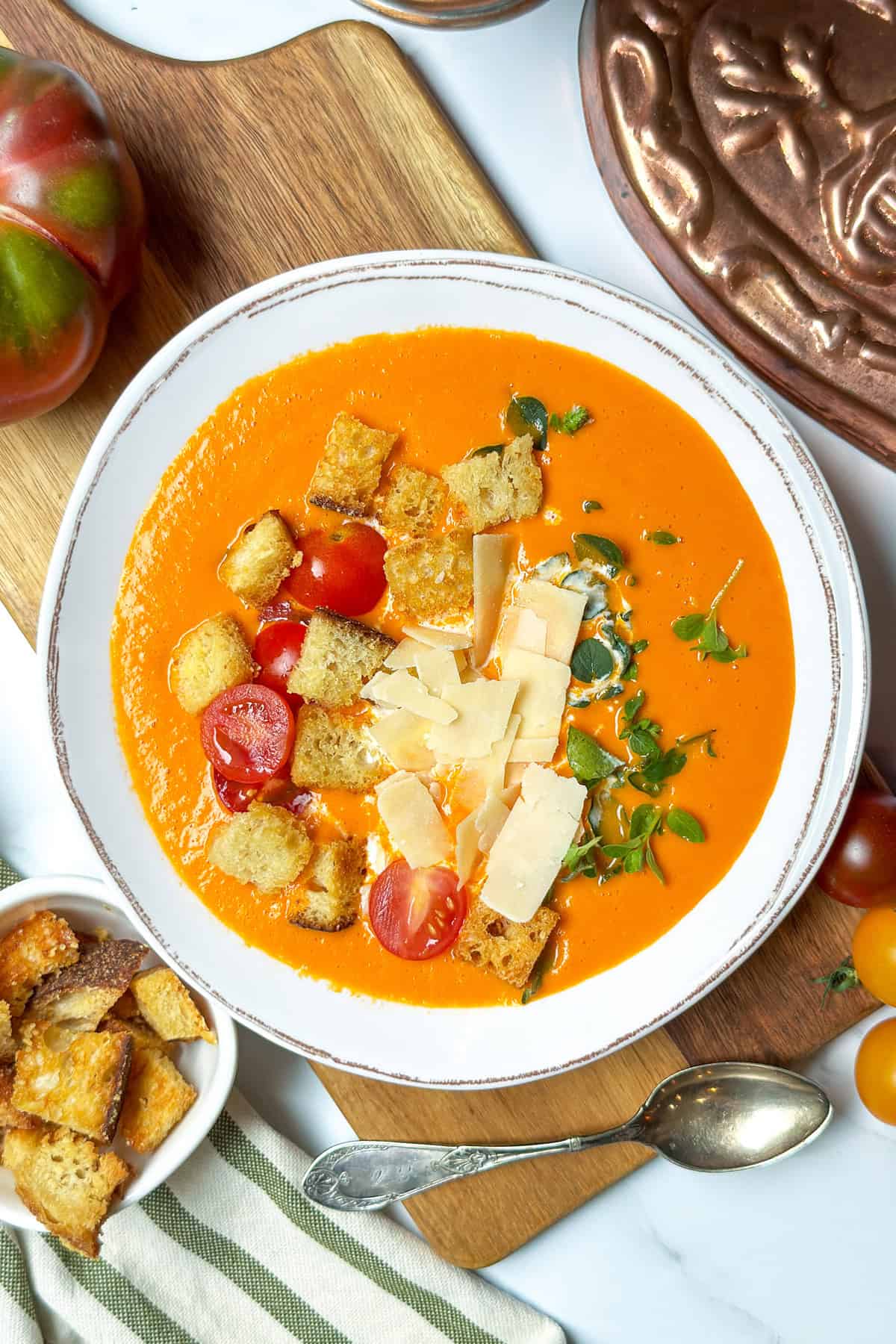 Creamy tomato soup in a white bowl and toppings plus more on the side.
