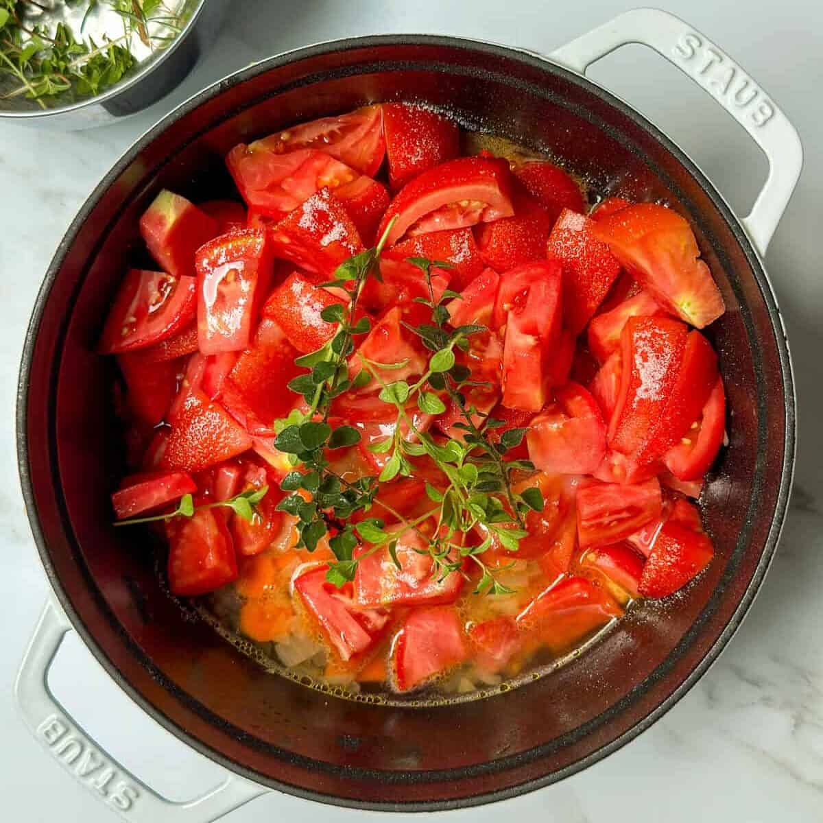 Fresh tomatoes and herbs along with sauteed carrots and onions in a large soup pot.