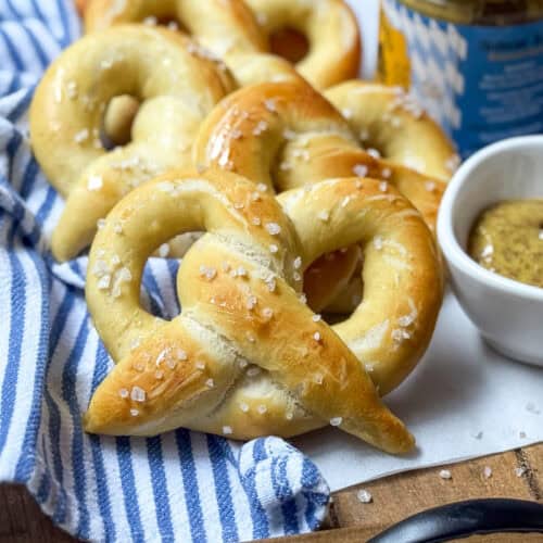 Six homemade pretzels lined up on a cloth and ready for serving.
