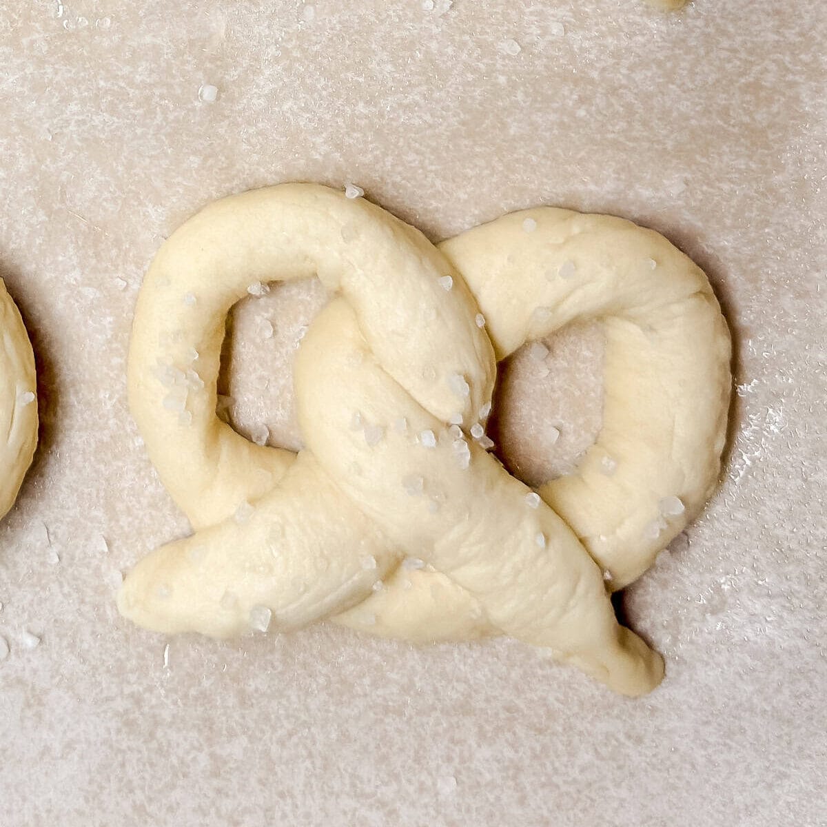 Shaped unbaked but boiled pretzel dough on a parchment lined baking sheet.
