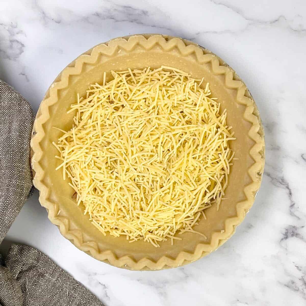 Shredded cheese over spinach in an unbaked pie crust for spinach quiche.