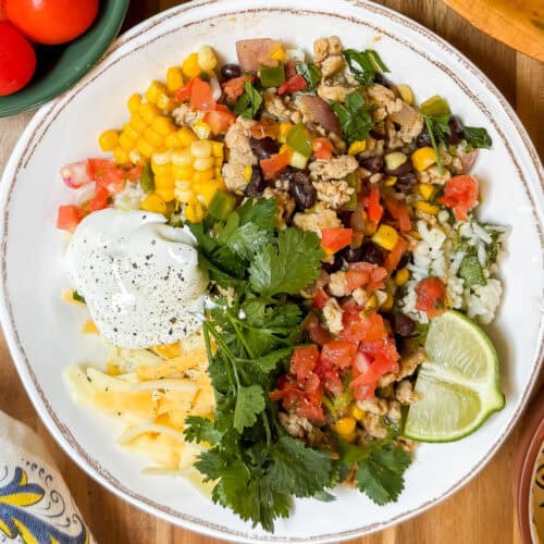 A bowl with rice, cooked ground meat, black beans, corn, shredded cheese, sour cream, pico de gallo, cilantro, and lime wedges-these taco bowls are bursting with fresh flavors.