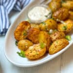 Close-up view of crispy air fryer potatoes with chopped green onions and herbs on a white plate with dipping sauce in the background.