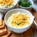 Bowl of creamy chicken potato chowder topped with shredded cheddar and parsley, served with crackers on the side.