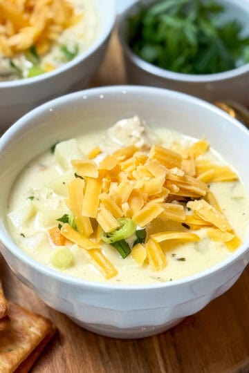 Bowl of creamy chicken potato chowder topped with shredded cheddar and parsley, served with crackers on the side.
