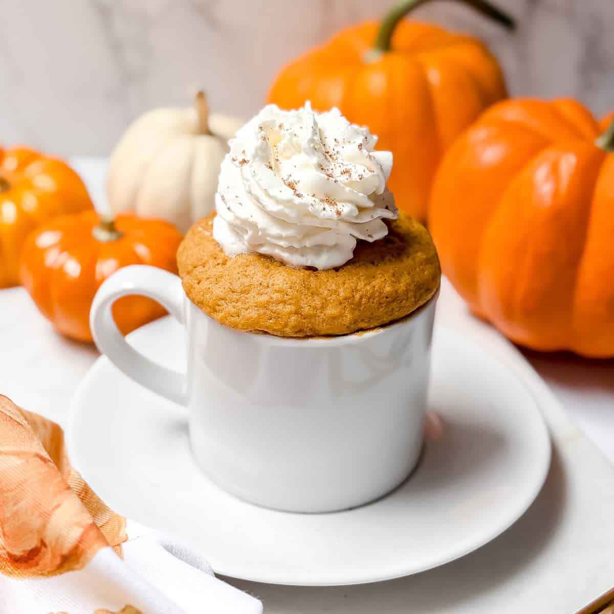 Just cooked microwave pumpkin mug cake topped with cinnamon dusted whipped cream.