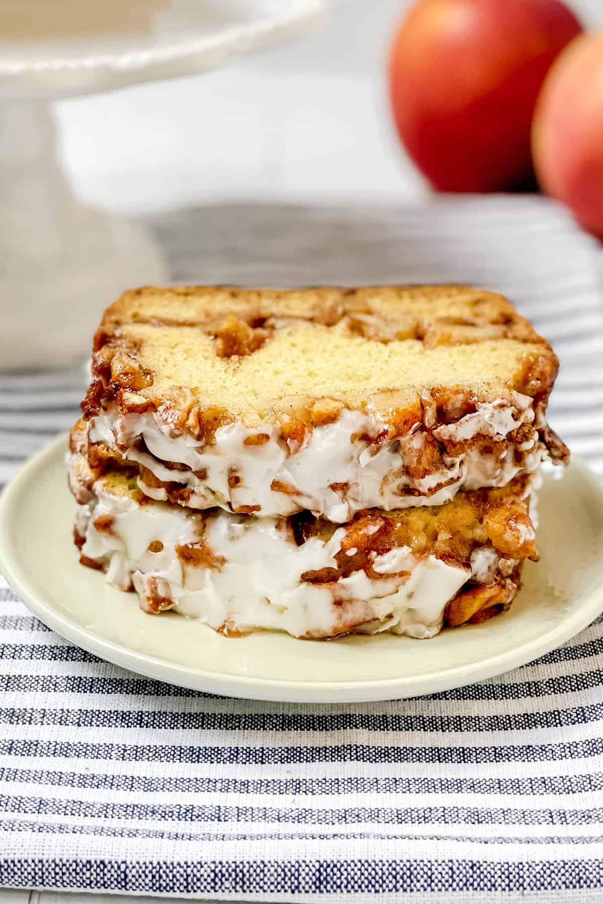 Two slices of apple fritter bread stacked on a white plate with the whole loaf in the background.