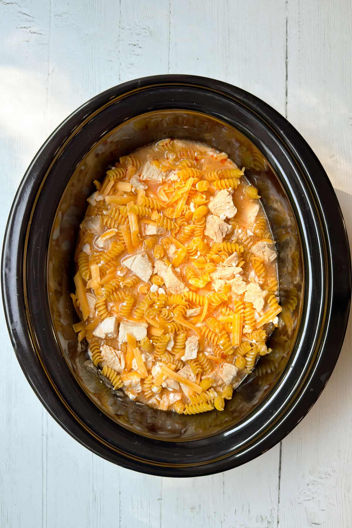 Uncooked rotini pasta, chicken, and shredded cheese added to the slow cooker.