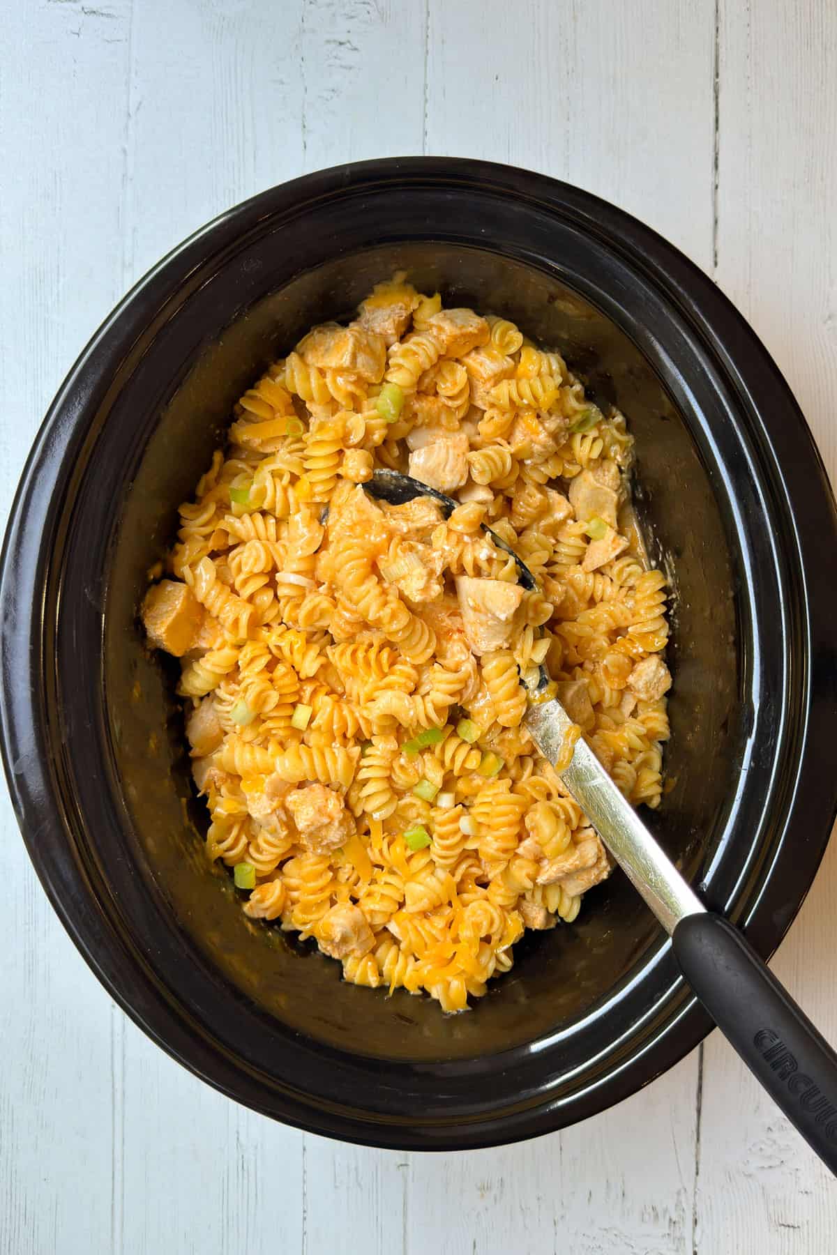 Buffalo chicken pasta being stirred in the slow cooker with melted cheese.