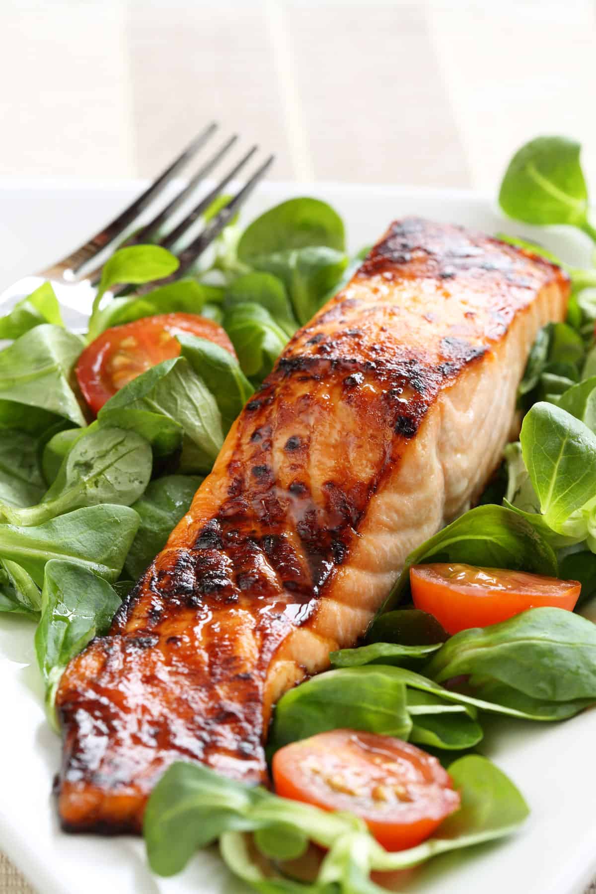 Filet of maple glazed salmon sitting on a bed of greens with cherry tomatoes.