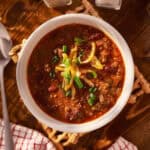 Bowl of 30 Minute Turkey Chili topped with shredded cheese and green onions, served on a rustic wooden table.