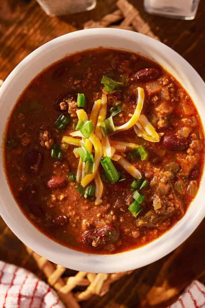 Bowl of 30 Minute Turkey Chili topped with shredded cheese and green onions, served on a rustic wooden table.