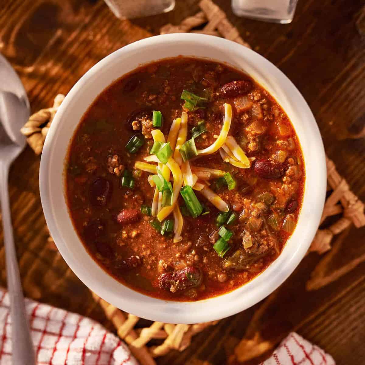 Bowl of 30 Minute Turkey Chili topped with shredded cheese and green onions, served on a rustic wooden table.
