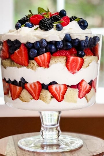 Square image of berry trifle with layers of fresh berries, chantilly cream, and fresh mint in a trifle dish ready for serving.