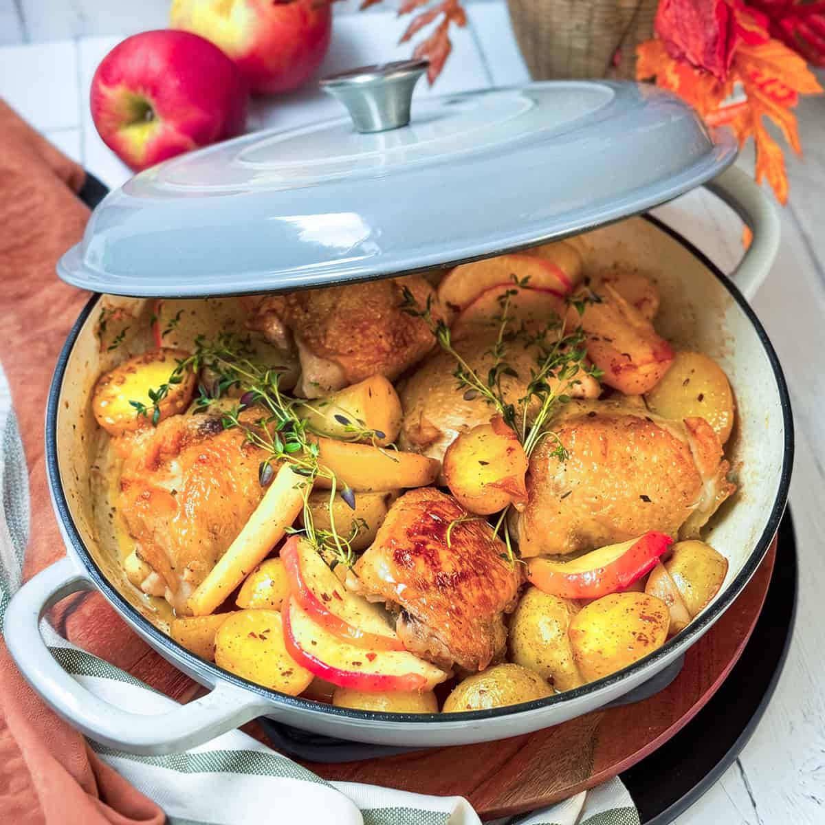 Chicken thighs roasting with root vegetables and potatoes in a braiser with creamy cider sauce.