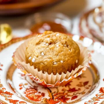 Close-up of a healthy apple muffin in a paper liner on a patterned fall plate, sprinkled with coarse sugar.
