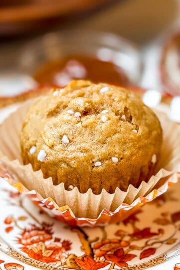Close-up of a healthy apple muffin in a paper liner on a patterned fall plate, sprinkled with coarse sugar.