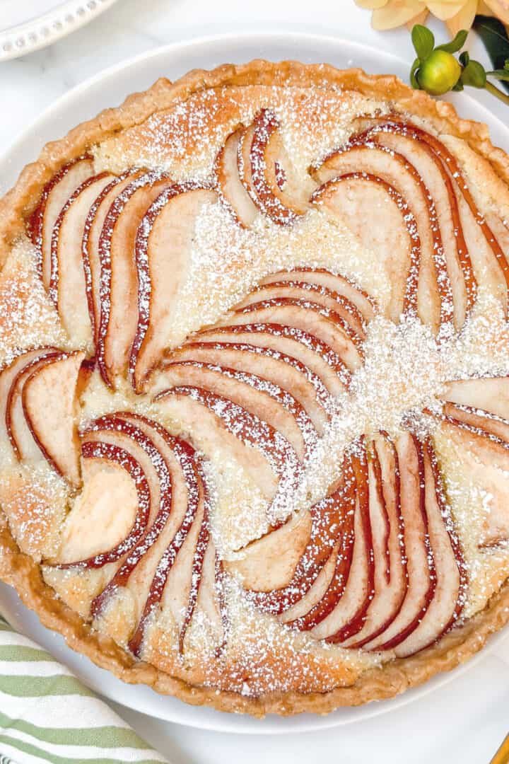 Overhead view of almond frangipane pear tart in a pastry crust, sprinkled with powdered sugar and styled with a gold server.