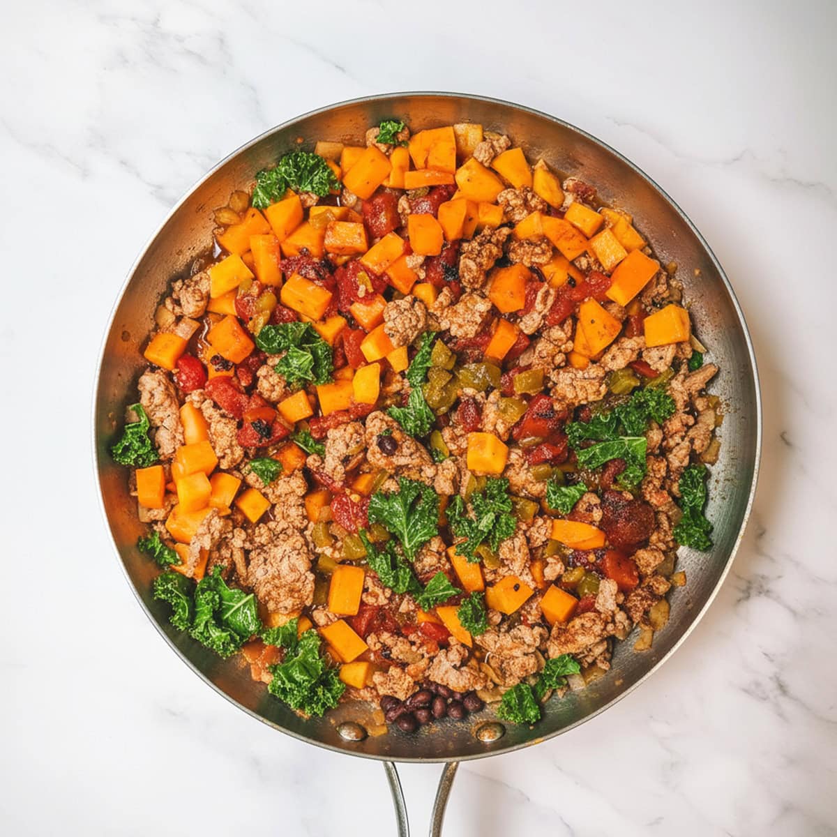 Adding tomatoes, black beans, and kale to the turkey butternut squash skillet meal.