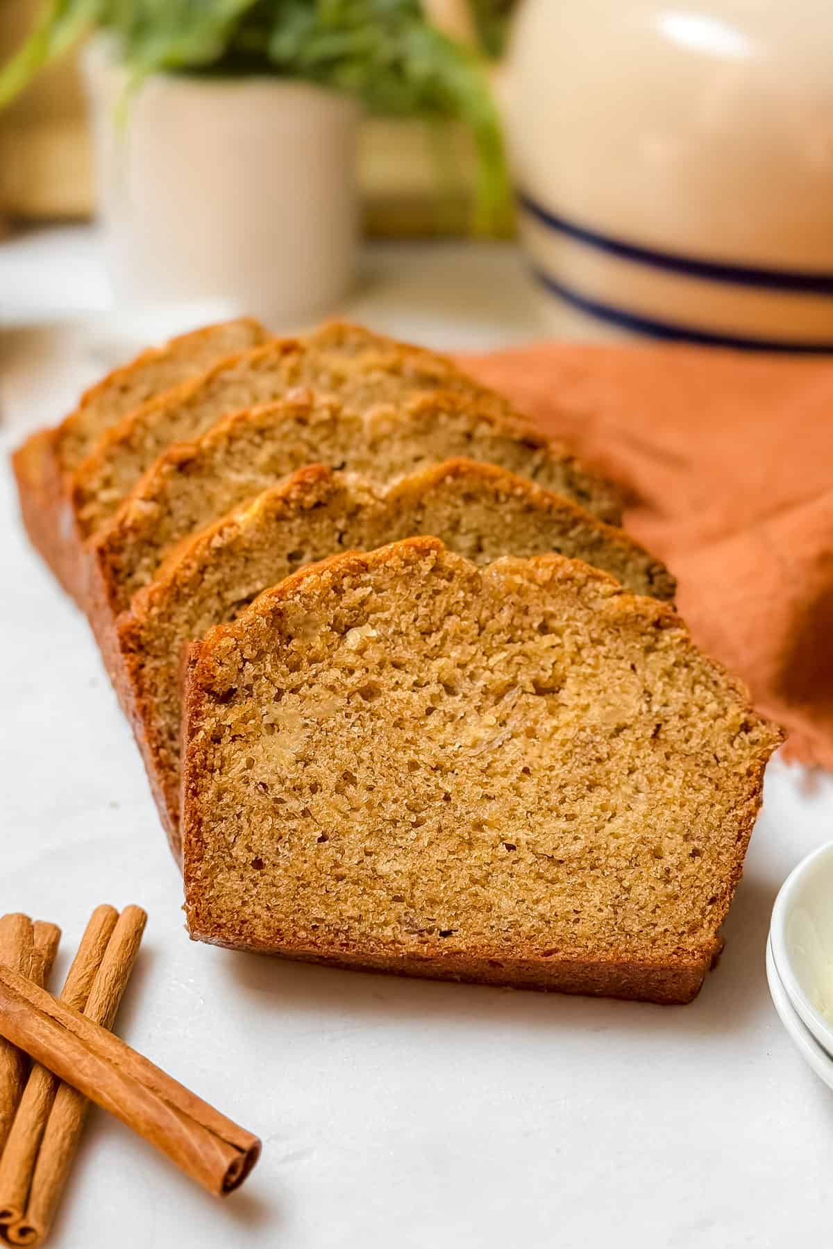Slices of baked banana bread on a white marble cutting board with cinnamon sticks nearby.