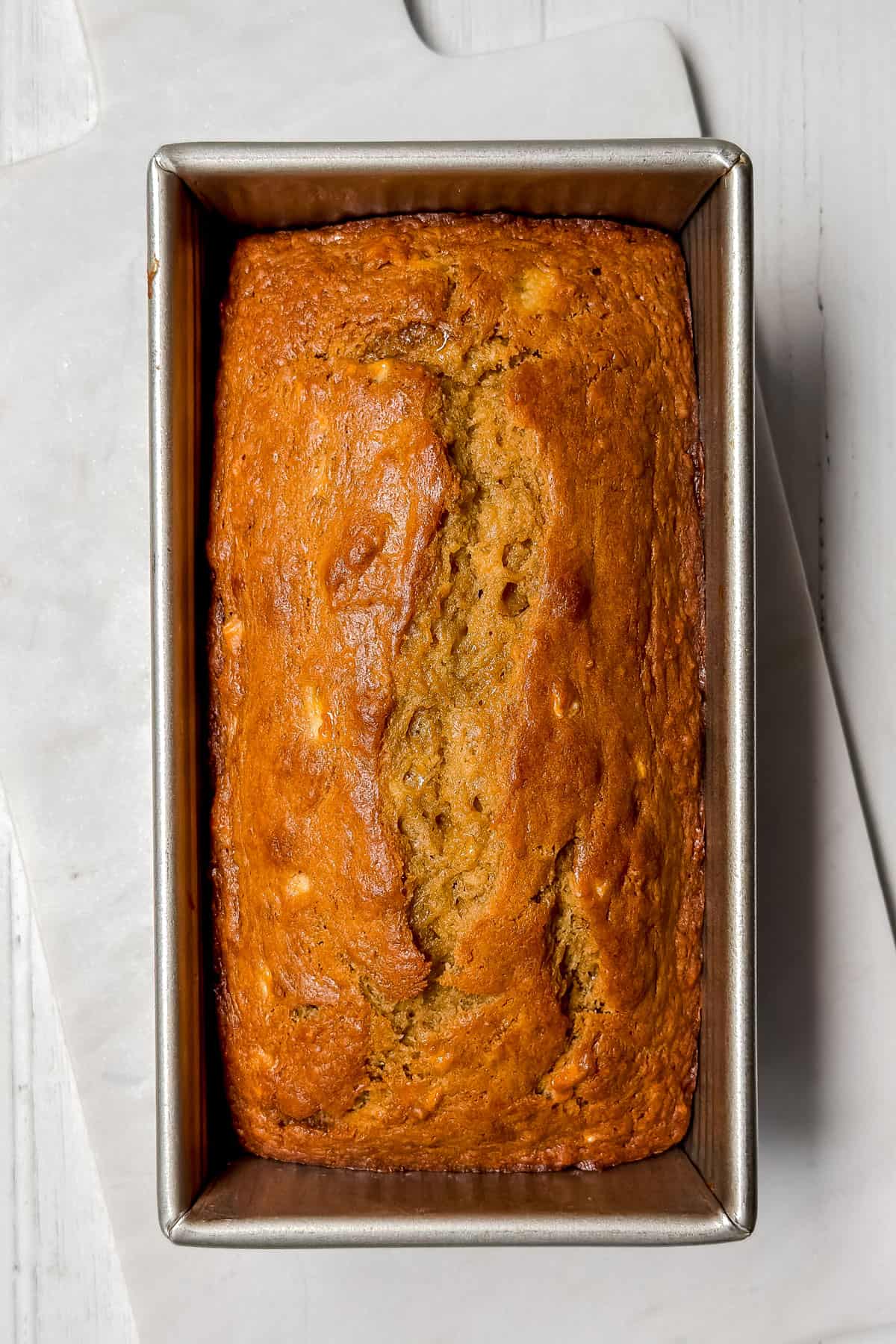 Just baked banana bread cooling on the counter in a steel loaf pan.
