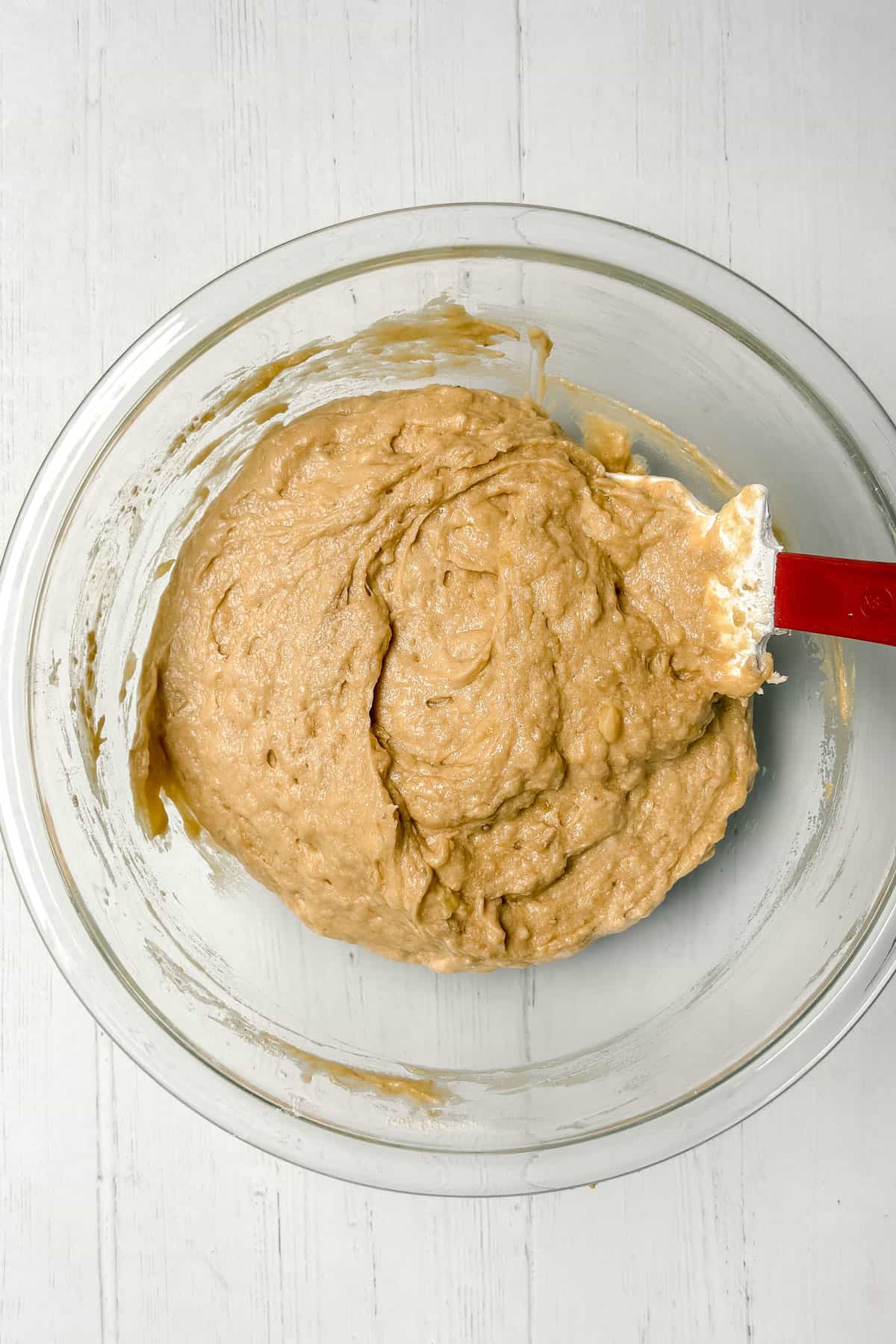 Mixing wet ingredients and dry ingredients together in a glass bowl to form a banana bread batter.