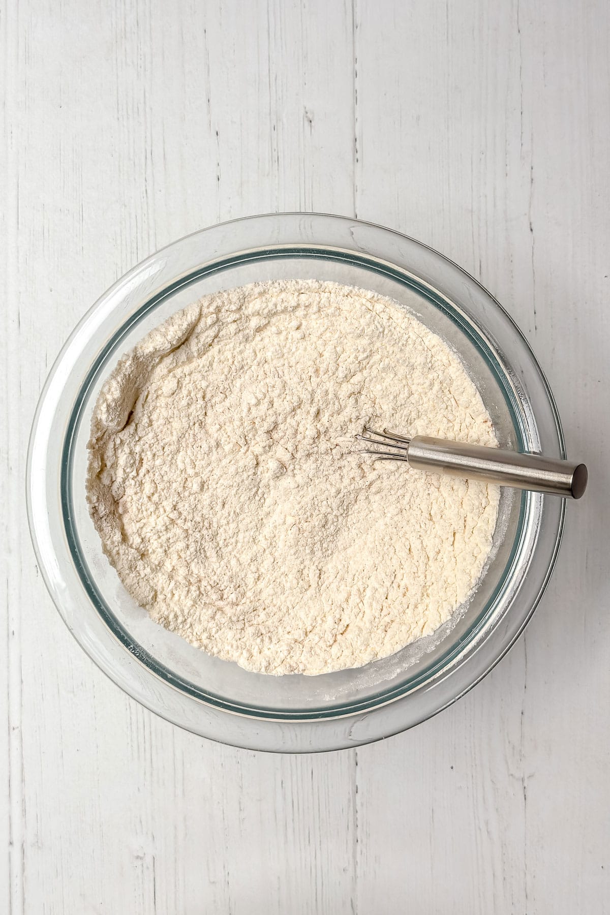 Whisking dry ingredients of flour, baking soda, salt, and cinnamon in a glass bowl with a whisk.