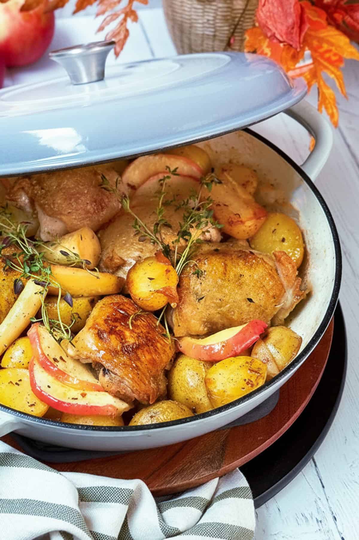 Chicken thighs roasting with root vegetables and potatoes in a braiser with creamy cider sauce.