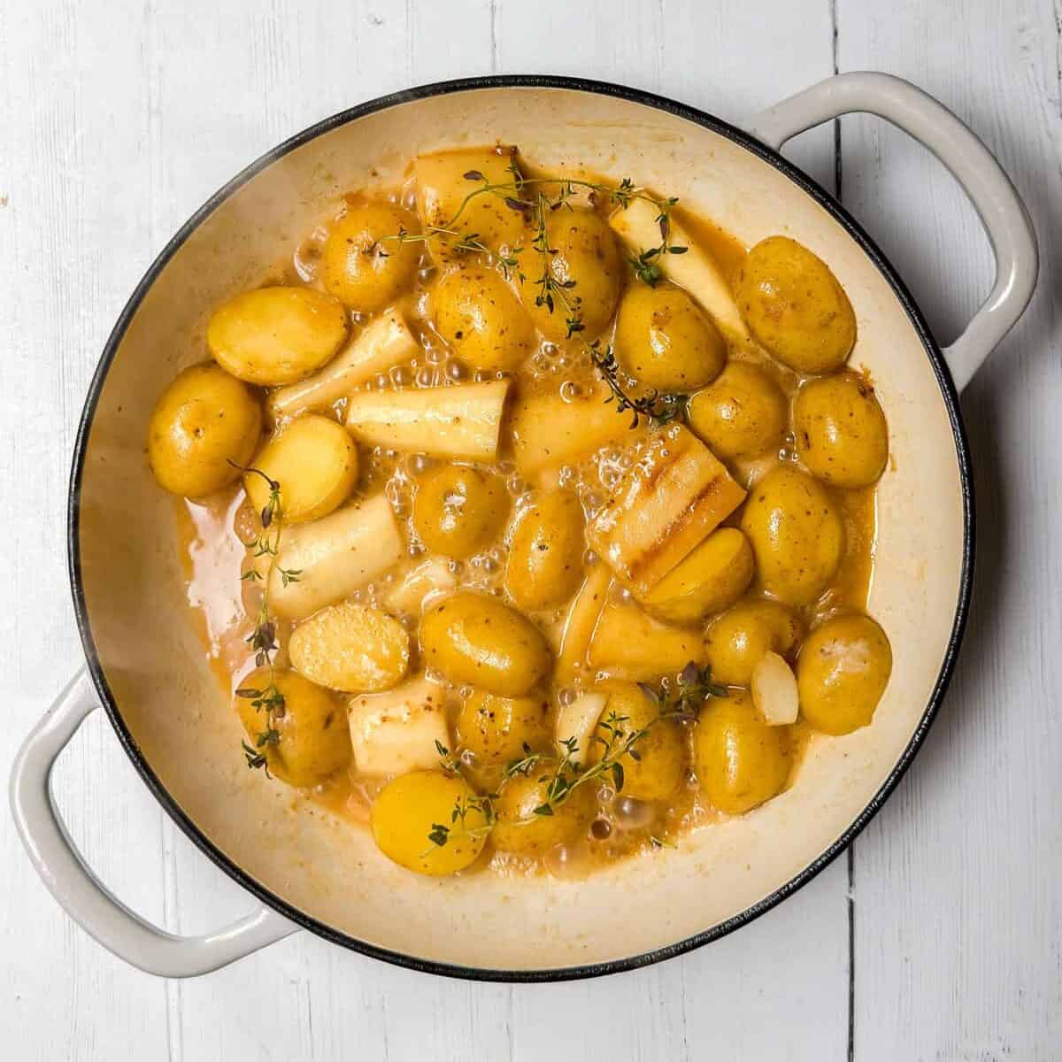 Sauteed root vegetables of potatoes, parsnips, and fresh herbs sauteed in a braising pot ready for  cooking with the chicken.