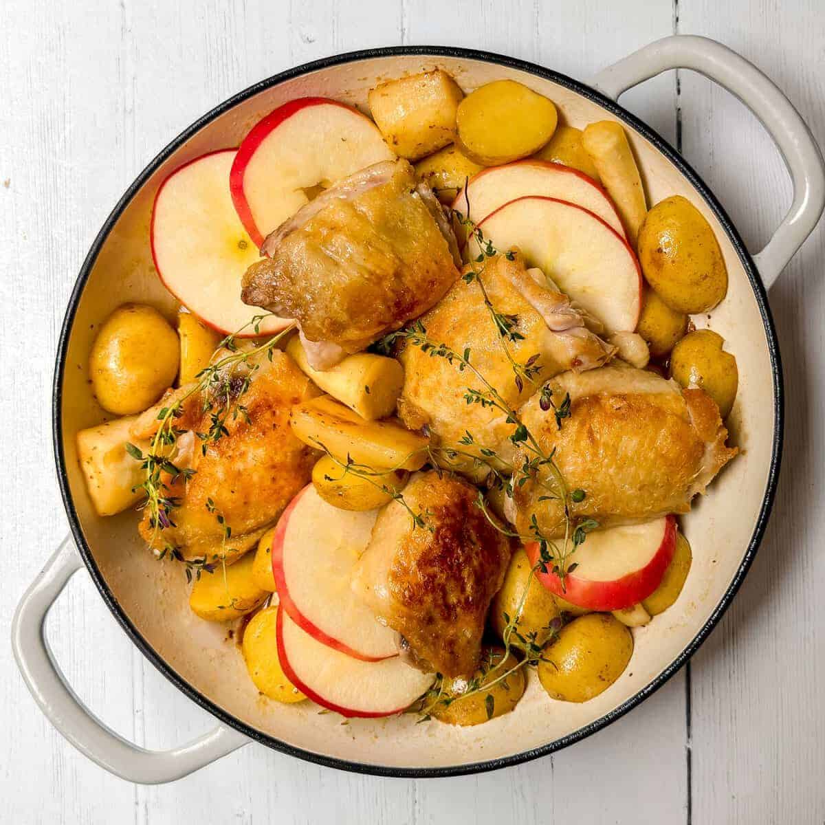 Browned chicken added to the pot along with fresh apple slices ready for baking.