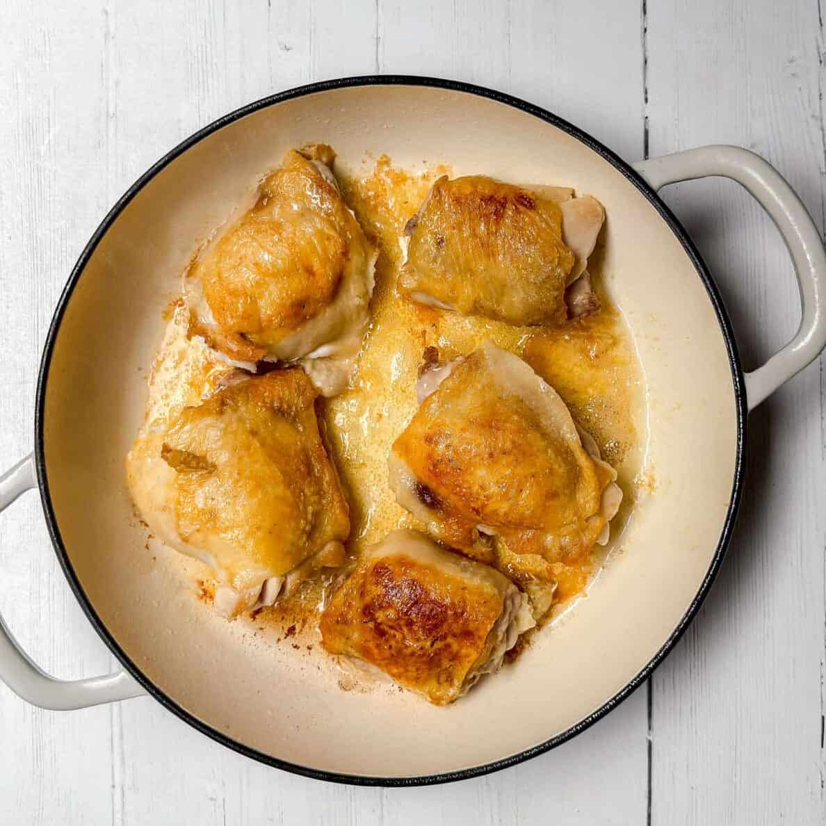 Seasoned and browned chicken thighs in a braising pot.