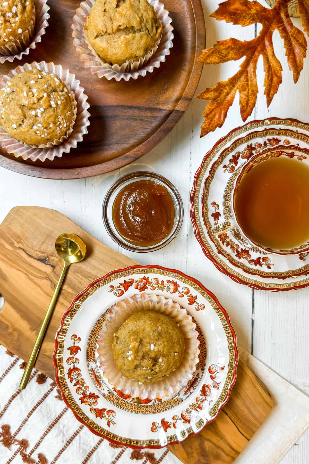 Table setting with healthy apple muffins, apple butter, and a cup of tea on autumn-themed china.