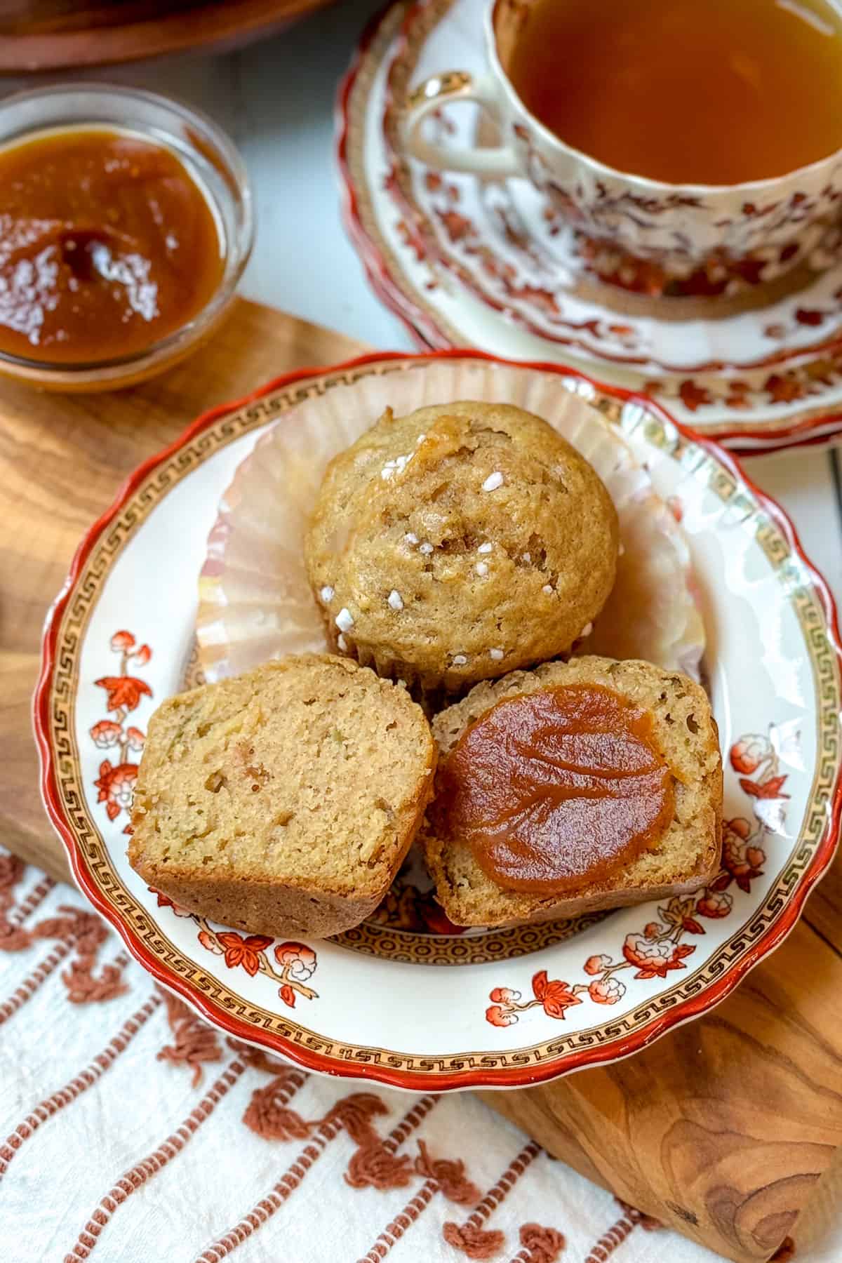 Sliced freshly baked healthy apple muffins on a patterned plate with apple butter on one half of the muffin.
