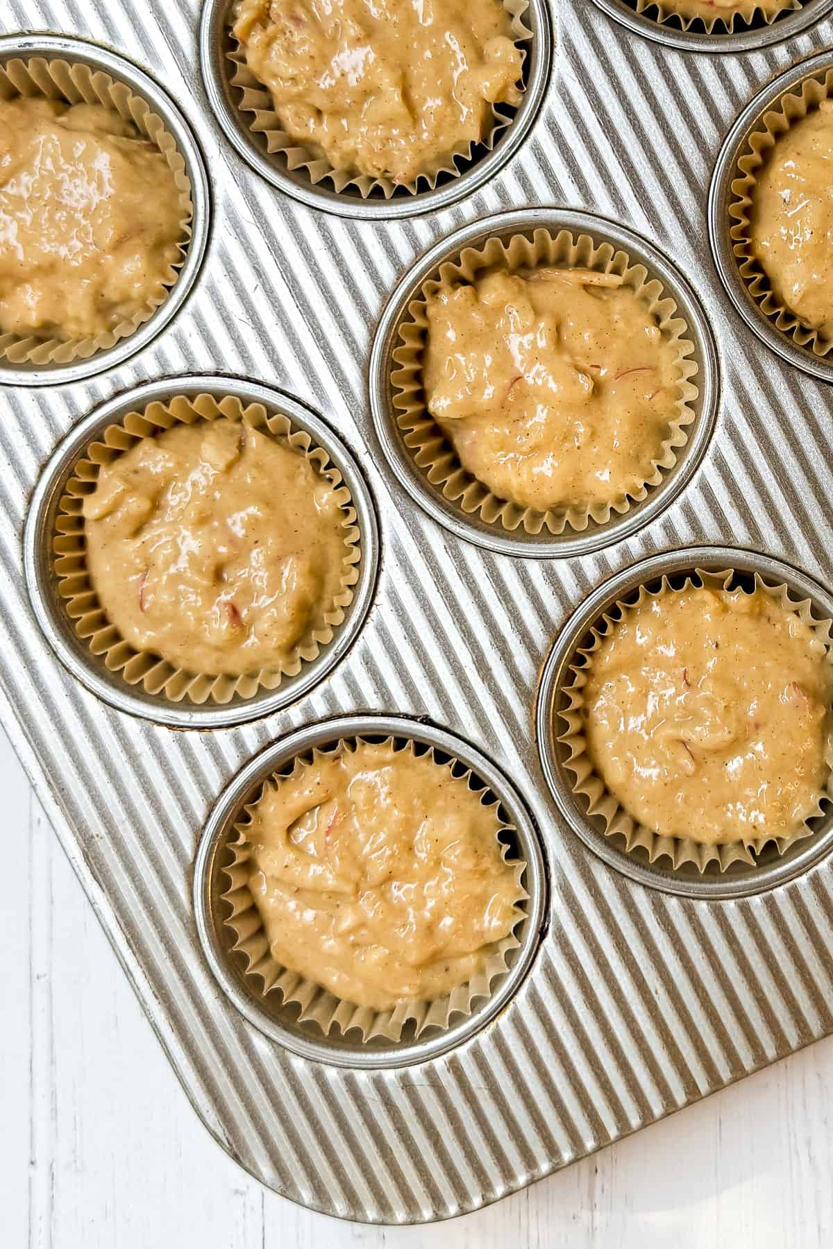 Muffin batter with shredded apple portioned into lined muffin tin cups.